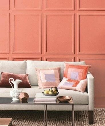koralų spalva ant sienos su smėlio spalvos sofa ir rausvomis pagalvėlėmis 